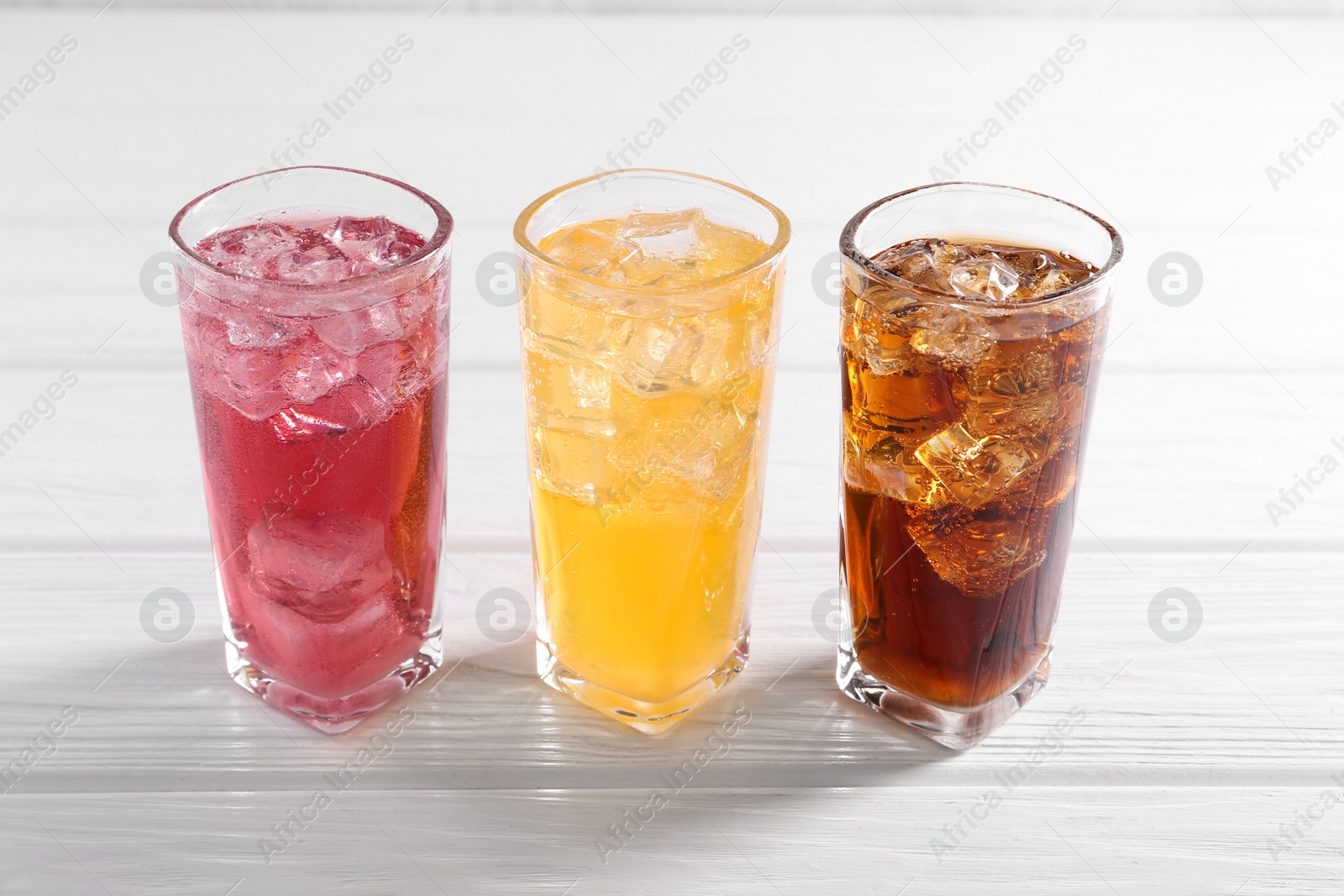 Photo of Soda water of different flavors with ice cubes in glasses on white wooden table