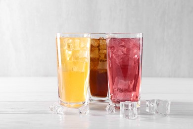 Photo of Soda water of different flavors in glasses with ice cubes on white wooden table