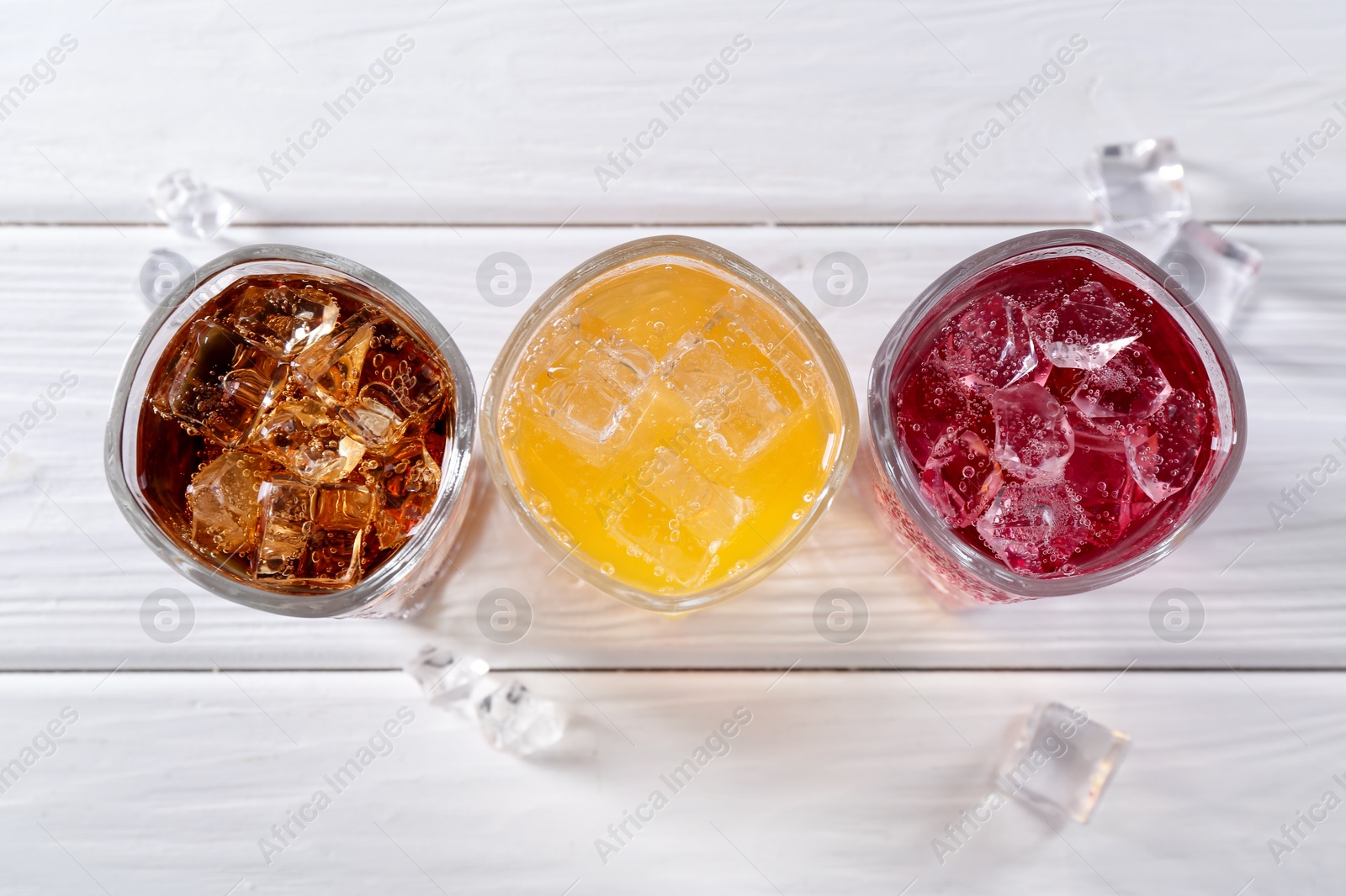 Photo of Soda water of different flavors in glasses with ice cubes on white wooden table, top view