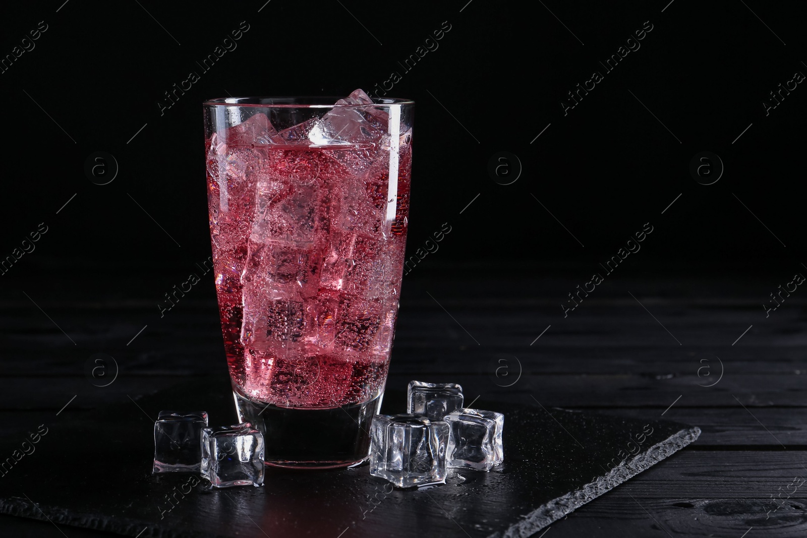 Photo of Sweet soda water in glass with ice cubes on black wooden table, space for text