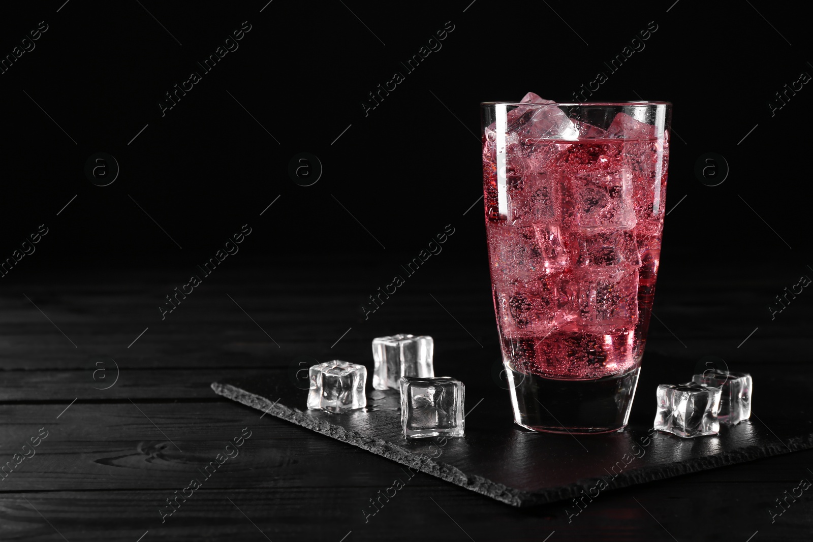 Photo of Sweet soda water in glass with ice cubes on black wooden table, space for text