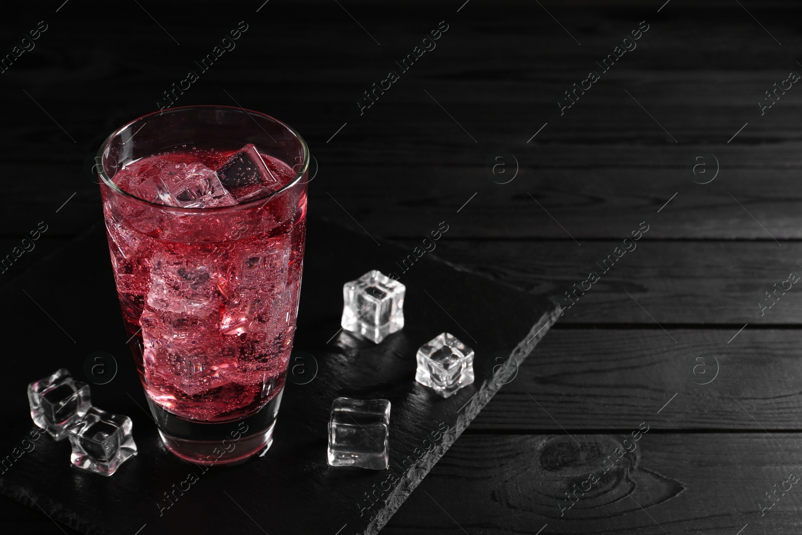 Photo of Sweet soda water in glass with ice cubes on black wooden table, space for text