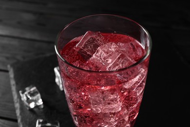 Photo of Sweet soda water with ice cubes in glass on black table, closeup