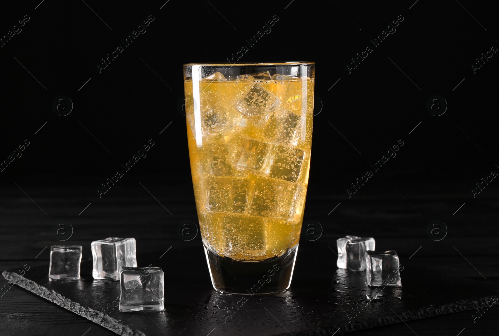 Photo of Sweet soda water in glass with ice cubes on black wooden table