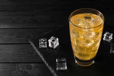 Photo of Sweet soda water in glass with ice cubes on black wooden table, space for text