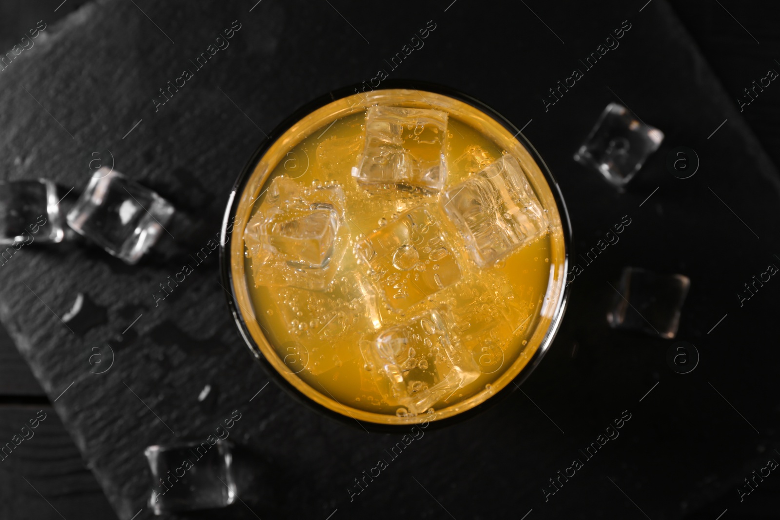 Photo of Sweet soda water with ice cubes in glass on black table, top view