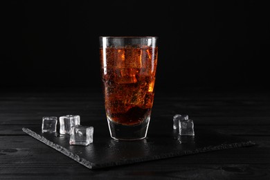 Photo of Sweet soda water in glass with ice cubes on black wooden table