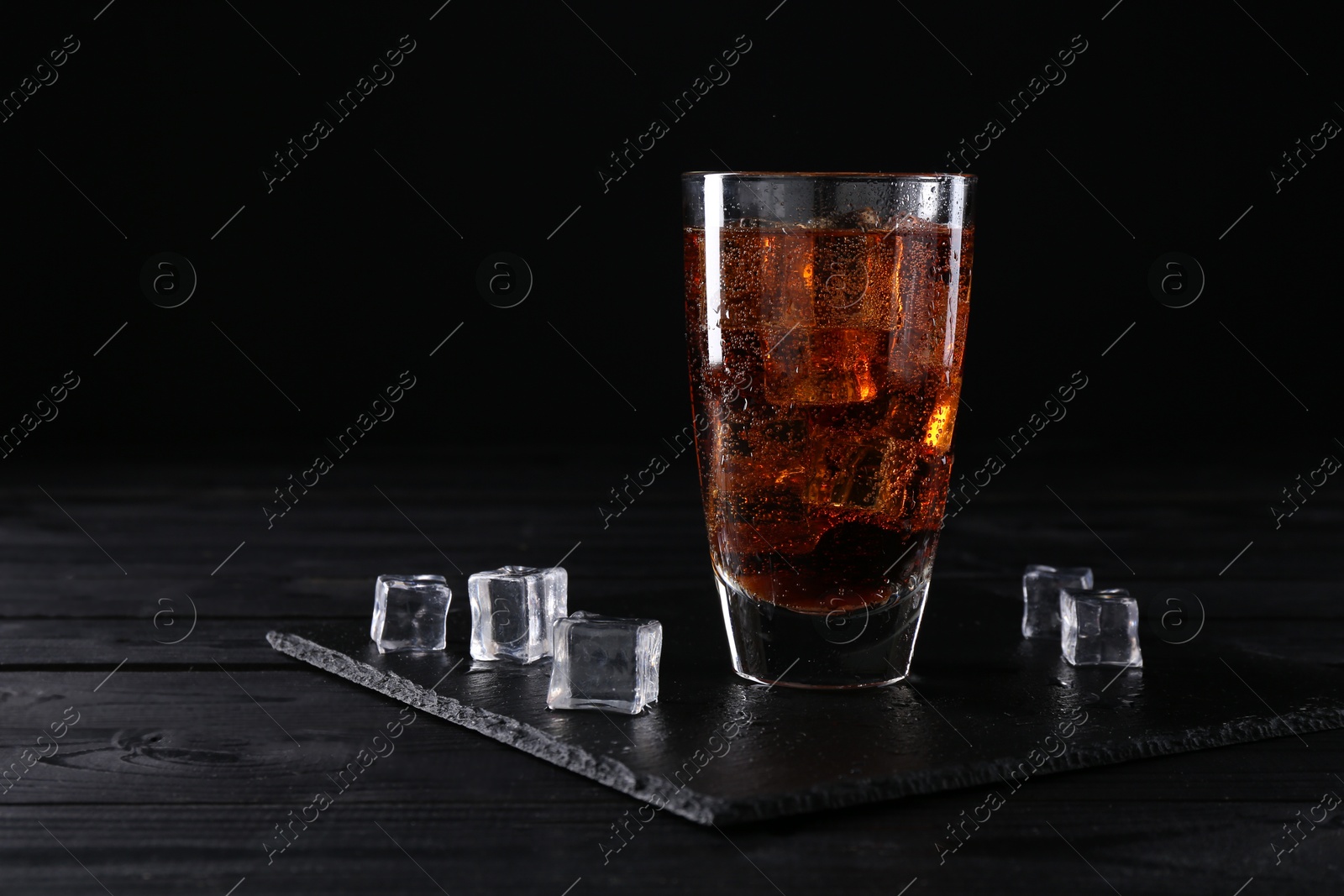 Photo of Sweet soda water in glass with ice cubes on black wooden table, space for text