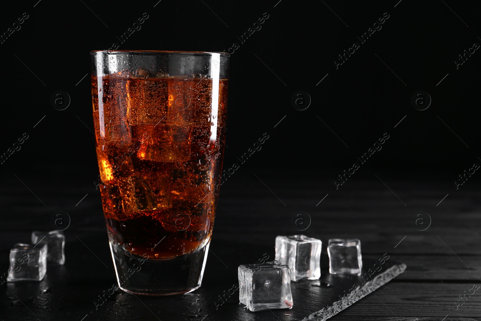 Photo of Sweet soda water in glass with ice cubes on black wooden table, space for text