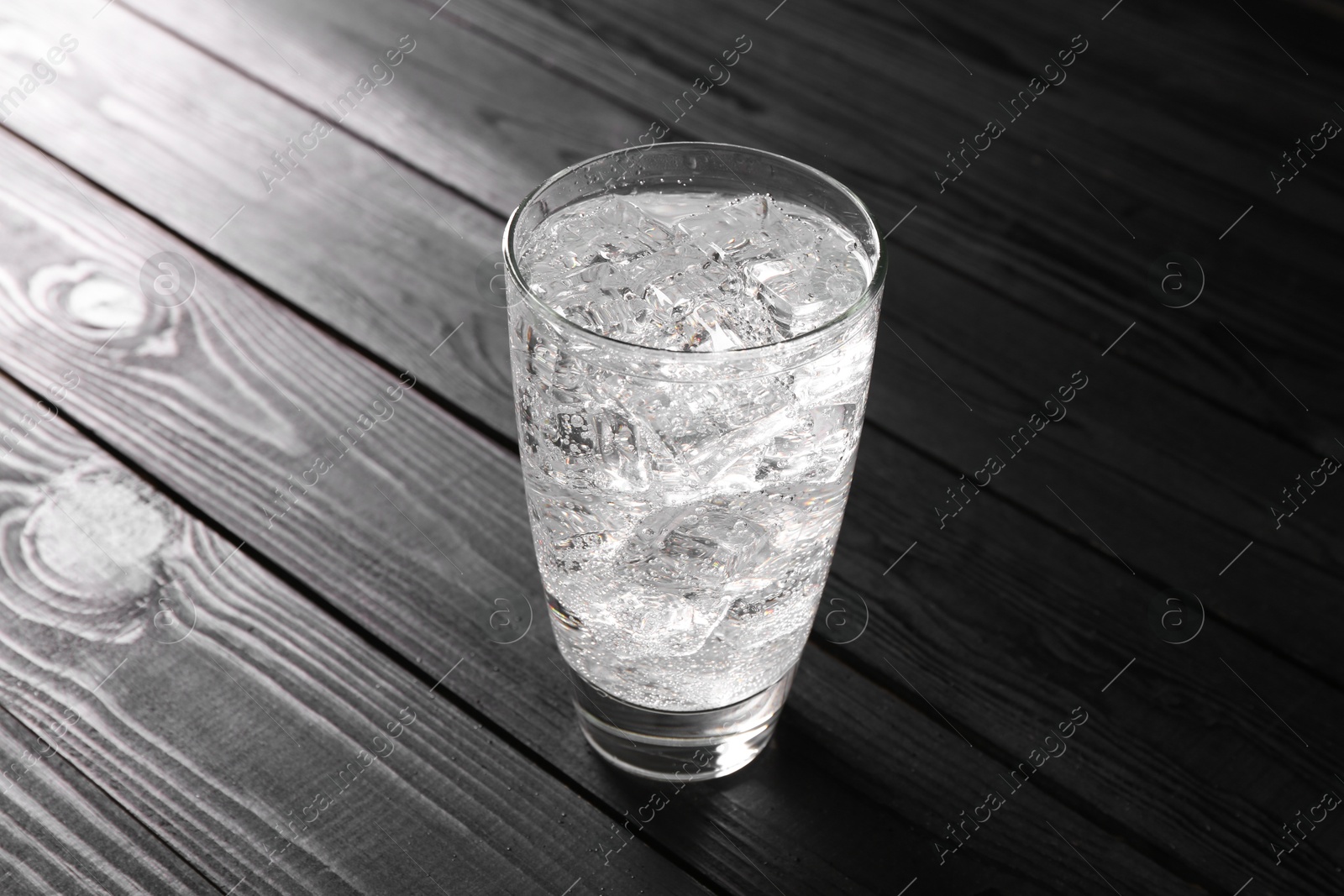 Photo of Refreshing soda water with ice cubes in glass on black wooden table, closeup