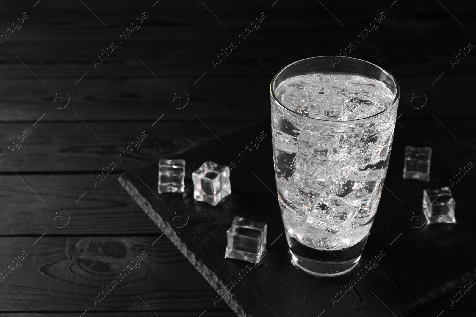 Photo of Refreshing soda water in glass with ice cubes on black wooden table, space for text