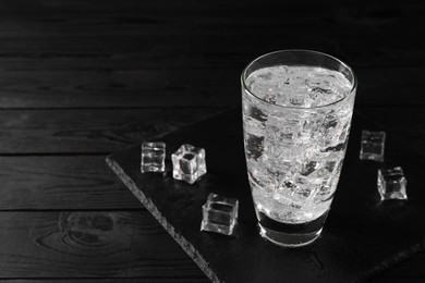 Photo of Refreshing soda water in glass with ice cubes on black wooden table, space for text