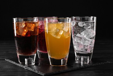 Photo of Refreshing soda water of different flavors with ice cubes in glasses on black wooden table