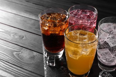 Photo of Refreshing soda water of different flavors in glasses with ice cubes on black wooden table, space for text