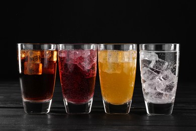 Photo of Refreshing soda water of different flavors with ice cubes in glasses on black wooden table