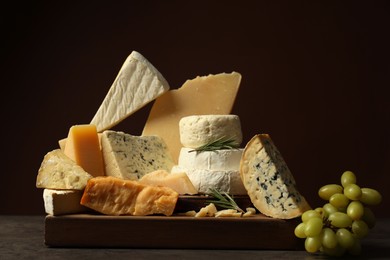 Photo of Different types of cheese, rosemary and grapes on grey table