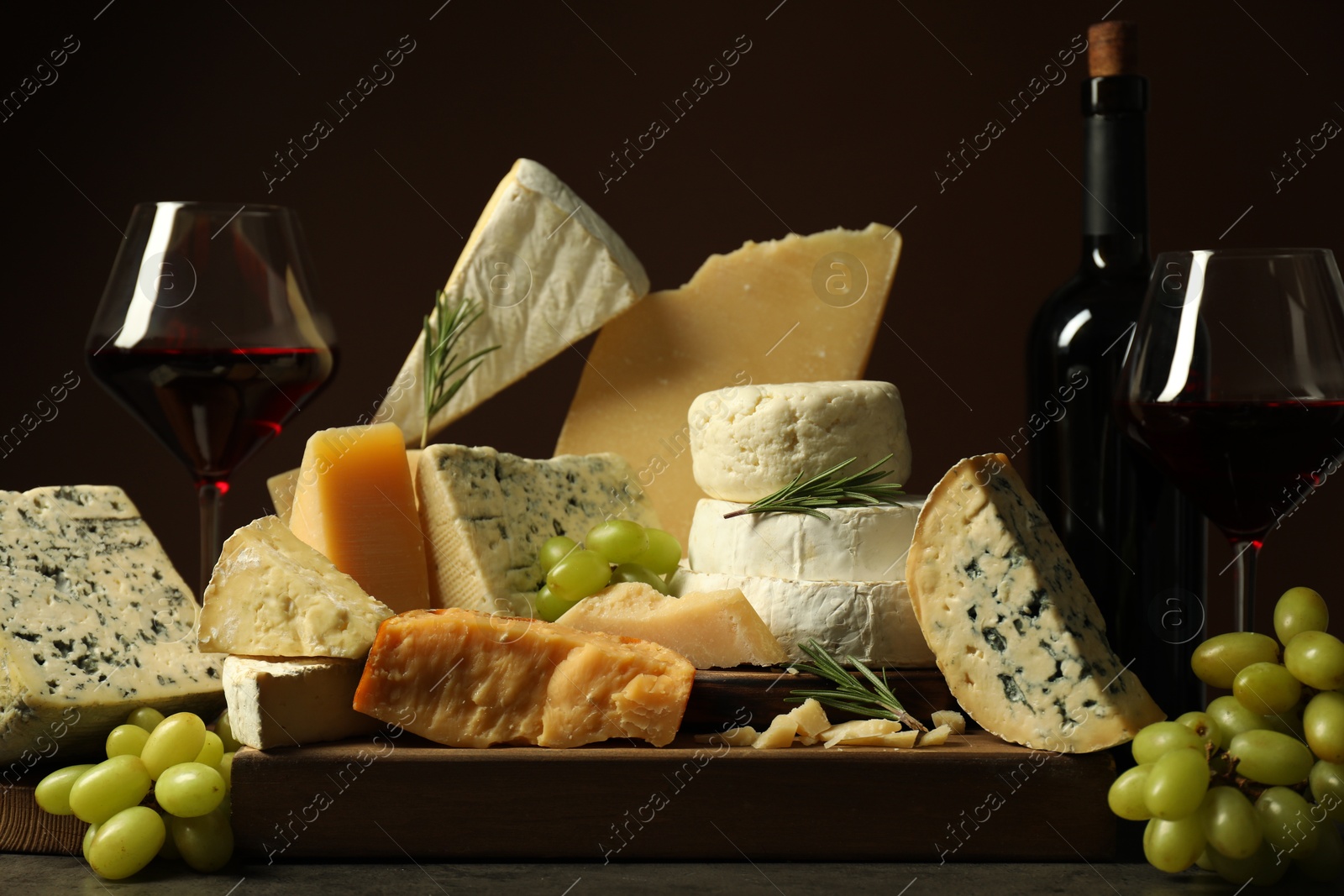 Photo of Different types of cheese, rosemary, grapes and wine on table