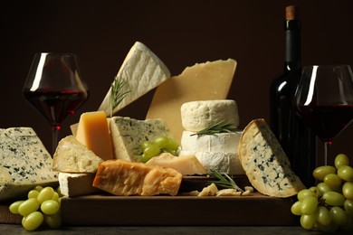 Photo of Different types of cheese, rosemary, grapes and wine on table