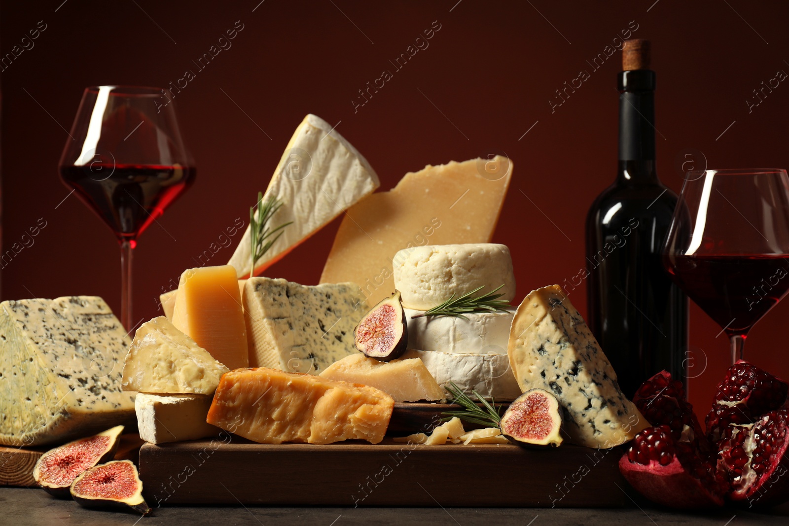 Photo of Different types of cheese, rosemary, figs, pomegranate and wine on table