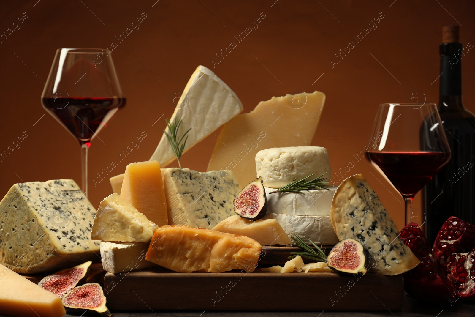 Photo of Different types of cheese, rosemary, figs, pomegranate and wine on table