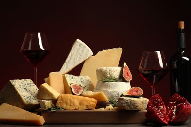 Photo of Different types of cheese, rosemary, figs, pomegranate and wine on table