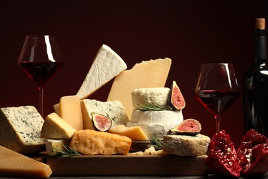 Photo of Different types of cheese, rosemary, figs, pomegranate and wine on table