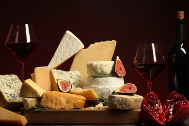 Photo of Different types of cheese, rosemary, figs, pomegranate and wine on table