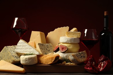 Photo of Different types of cheese, rosemary, fig, pomegranate and wine on table