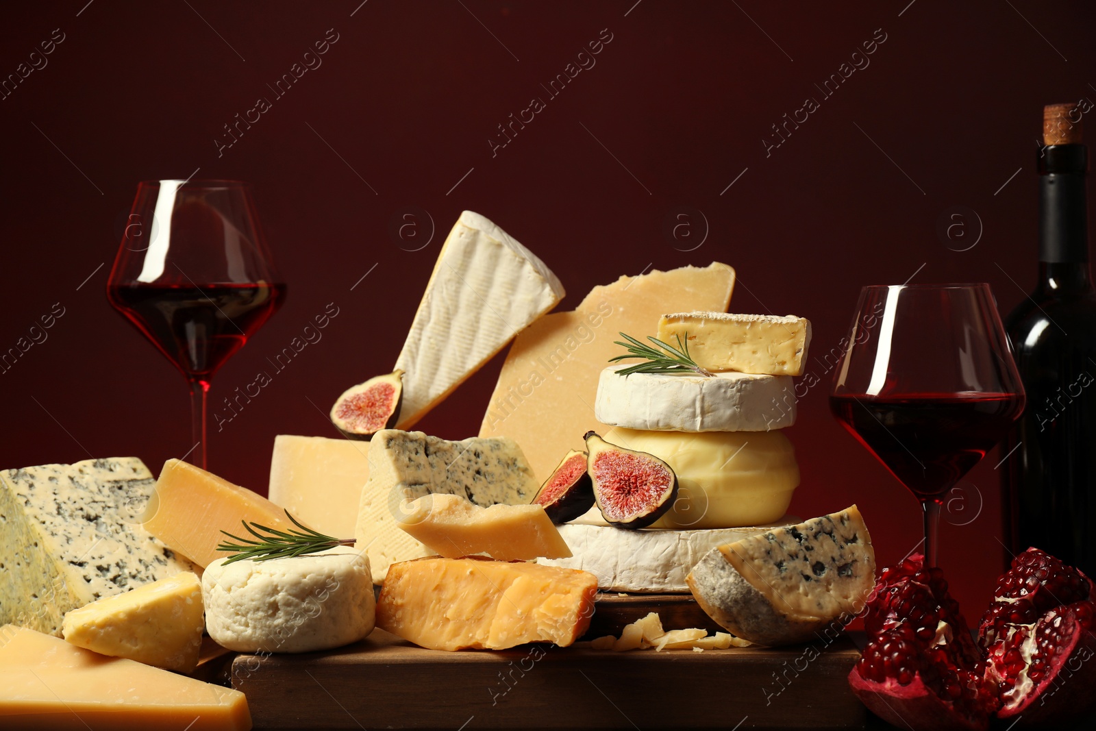 Photo of Different types of cheese, rosemary, figs, pomegranate and wine on table