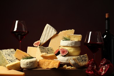 Photo of Different types of cheese, rosemary, figs, pomegranate and wine on table