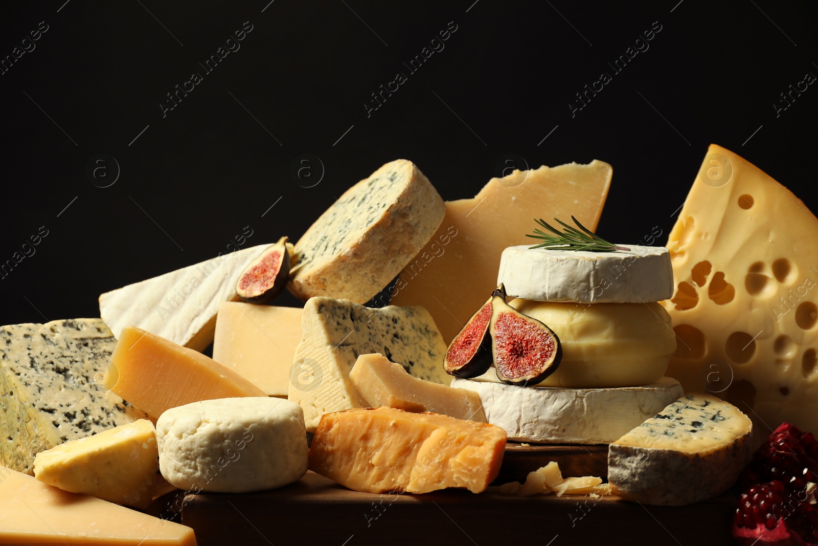 Photo of Different types of cheese, rosemary, figs and pomegranate on table