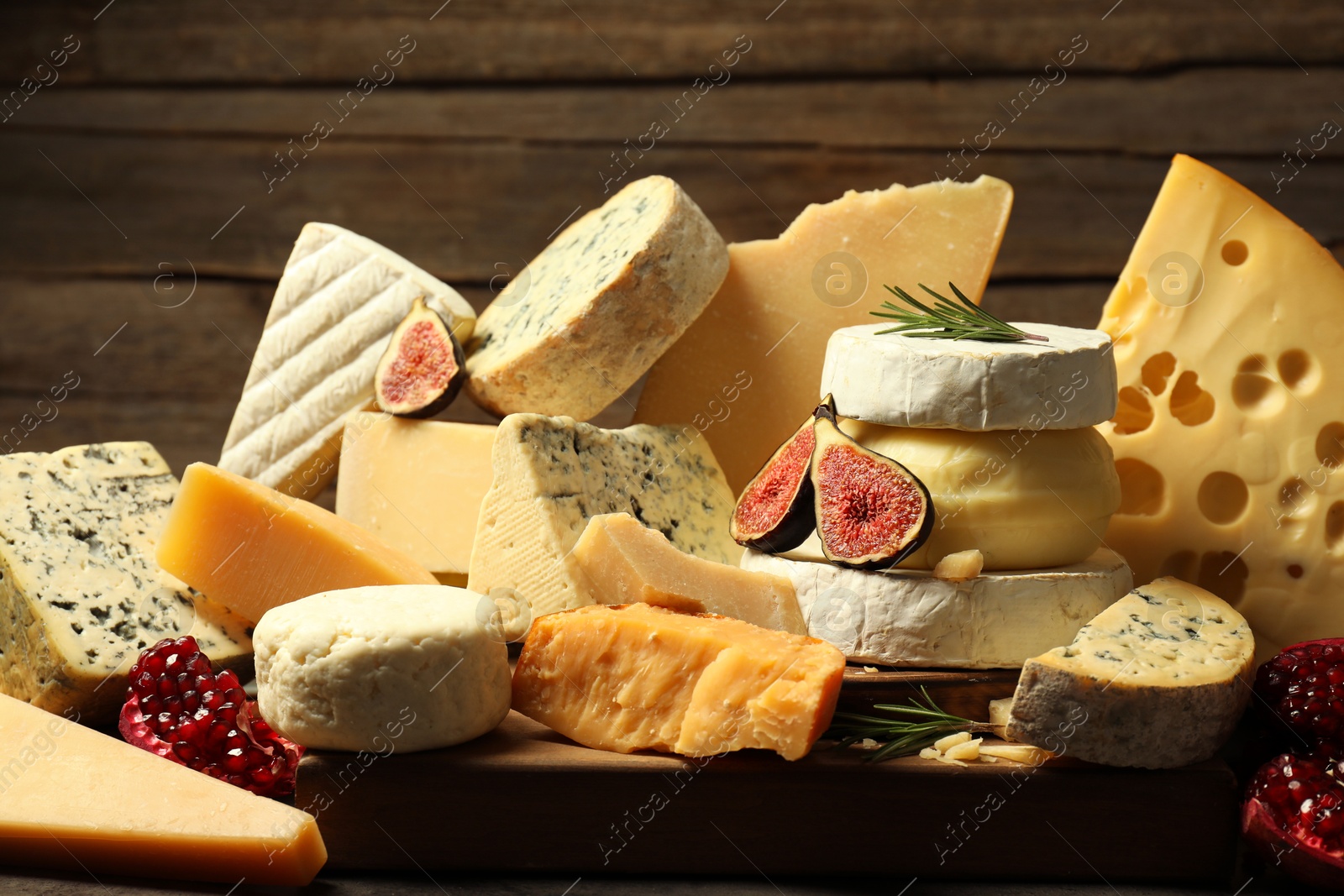 Photo of Different types of cheese, rosemary, figs and pomegranate on table