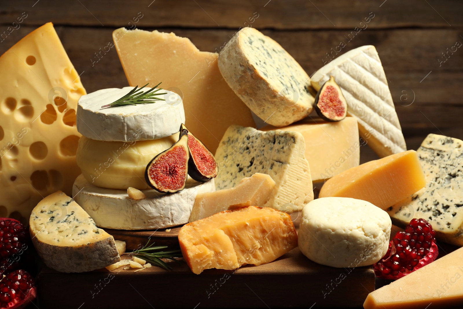 Photo of Different types of cheese, rosemary, figs and pomegranate on table