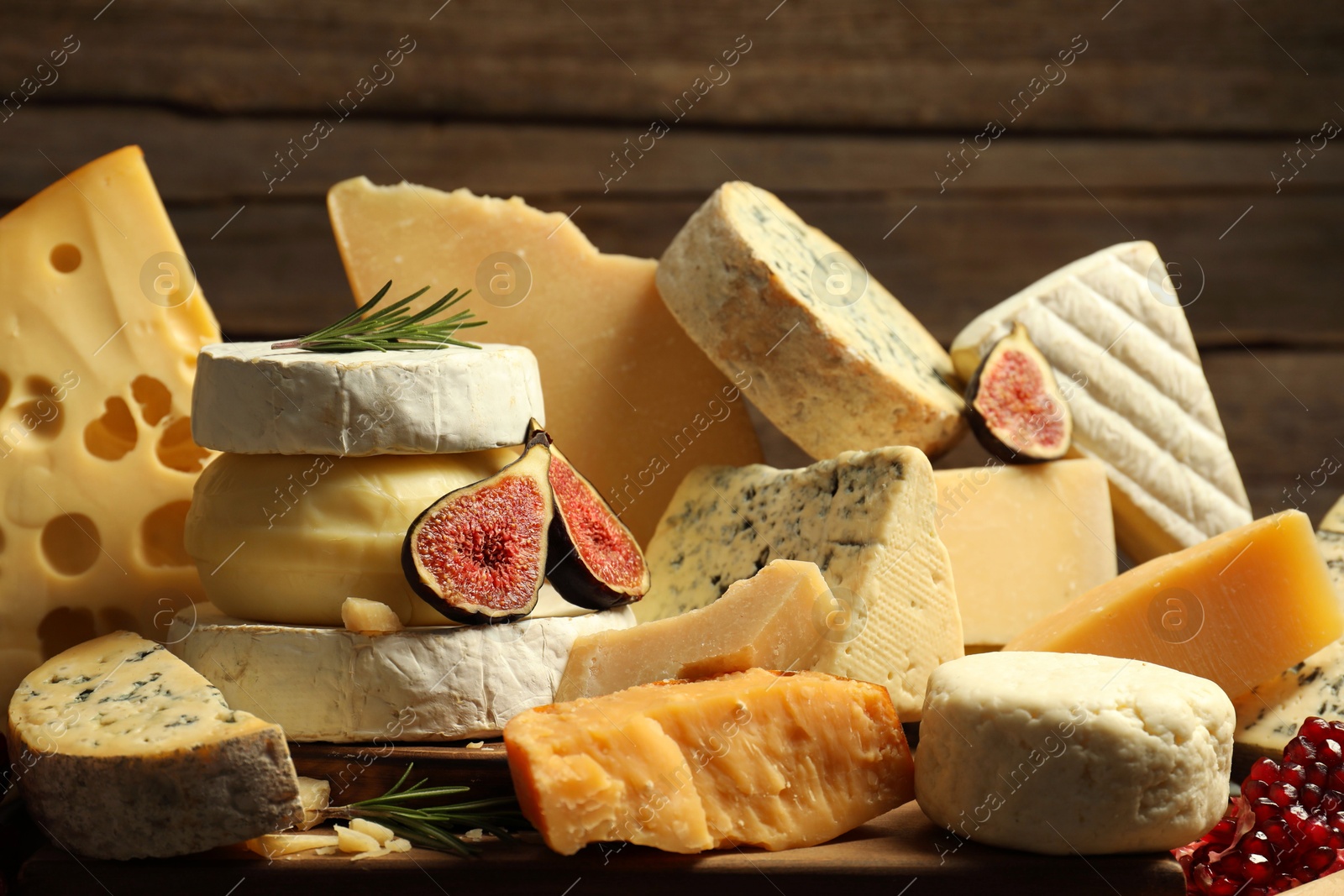 Photo of Different types of cheese, rosemary, figs and pomegranate on table