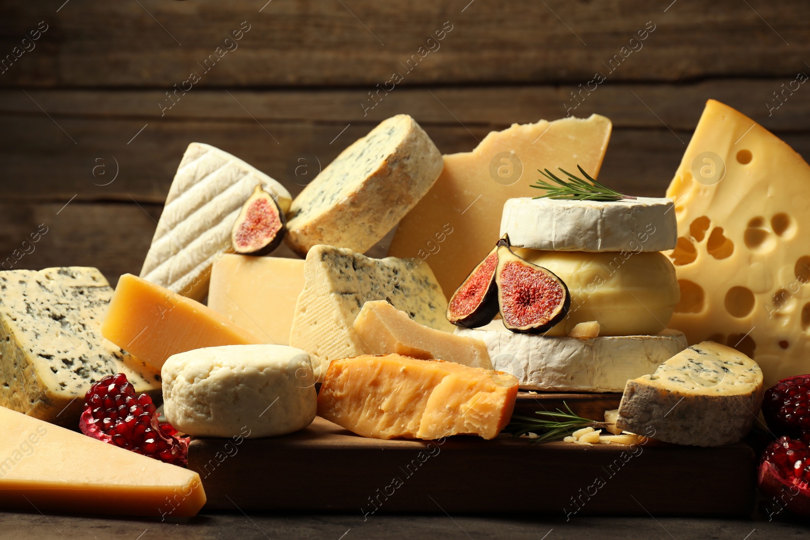 Photo of Different types of cheese, rosemary, figs and pomegranate on grey table