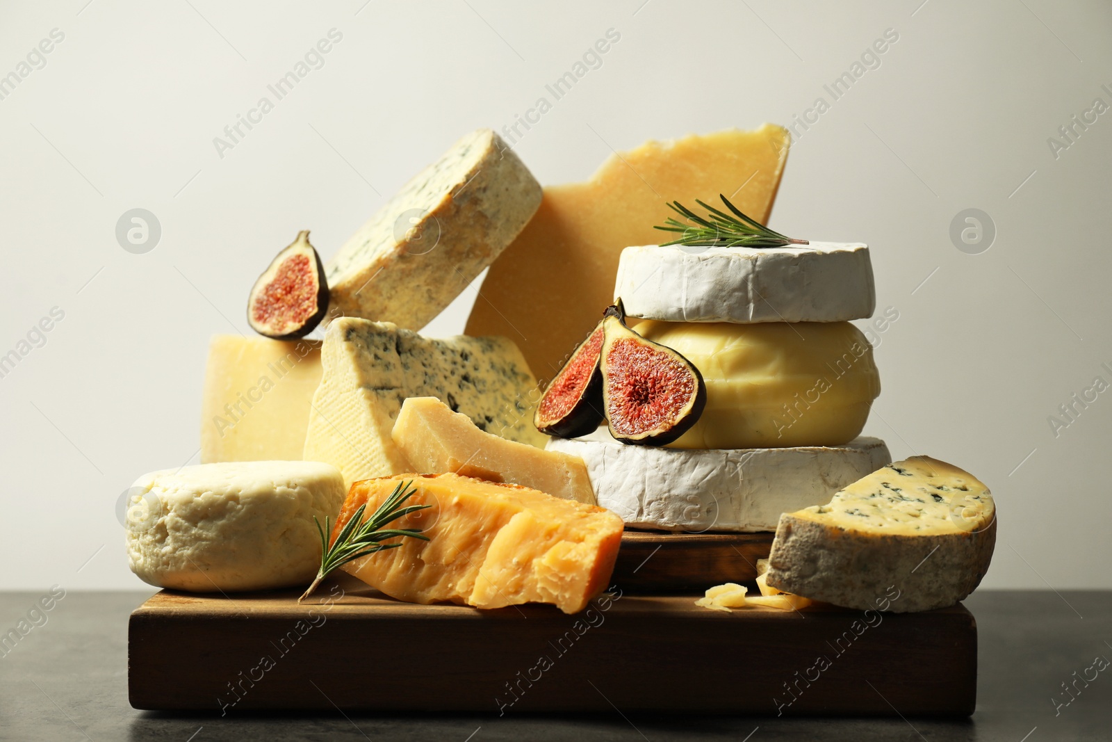 Photo of Different types of cheese, figs and rosemary on grey table