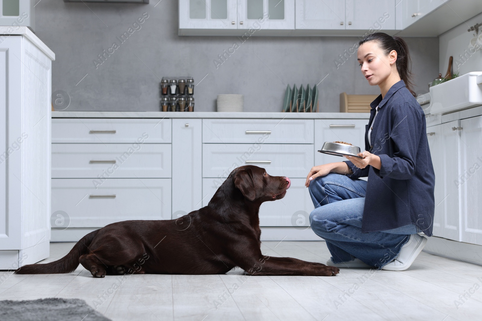 Photo of Woman giving bowl with dry pet food to her dog indoors