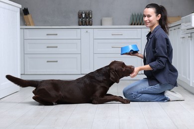 Photo of Woman with feeding bowl giving dry pet food to her dog indoors