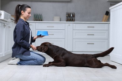 Photo of Woman with feeding bowl giving dry pet food to her dog indoors