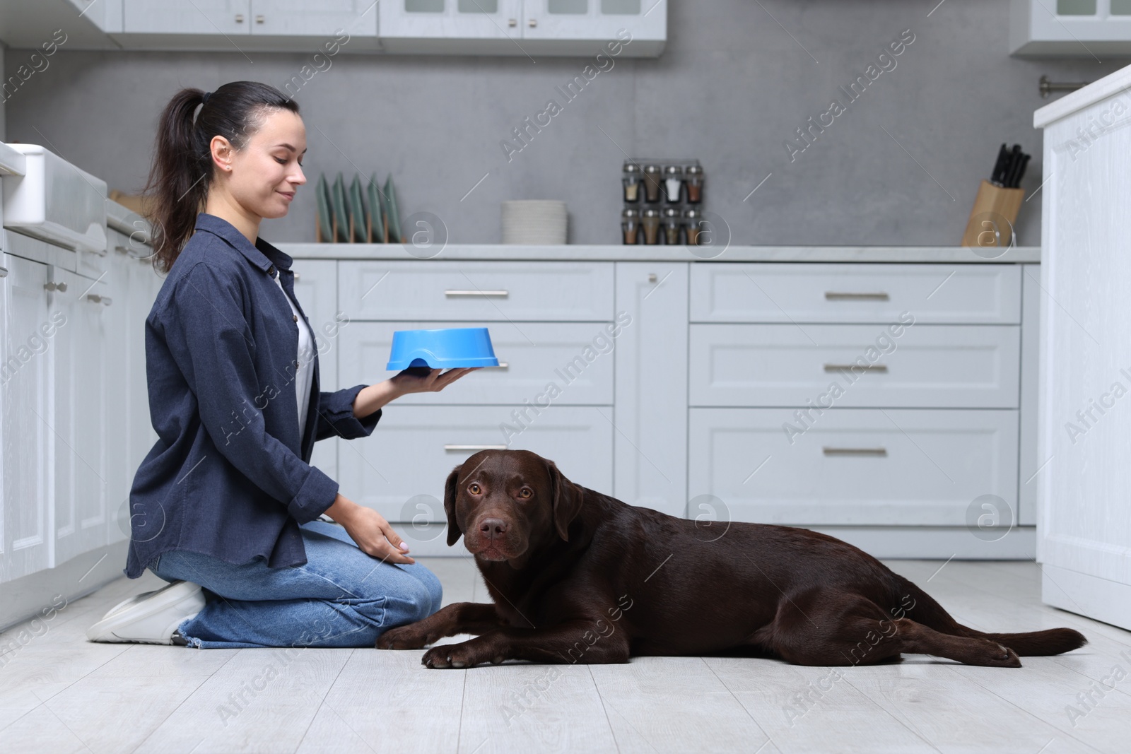 Photo of Woman with feeding bowl giving dry pet food to her dog indoors