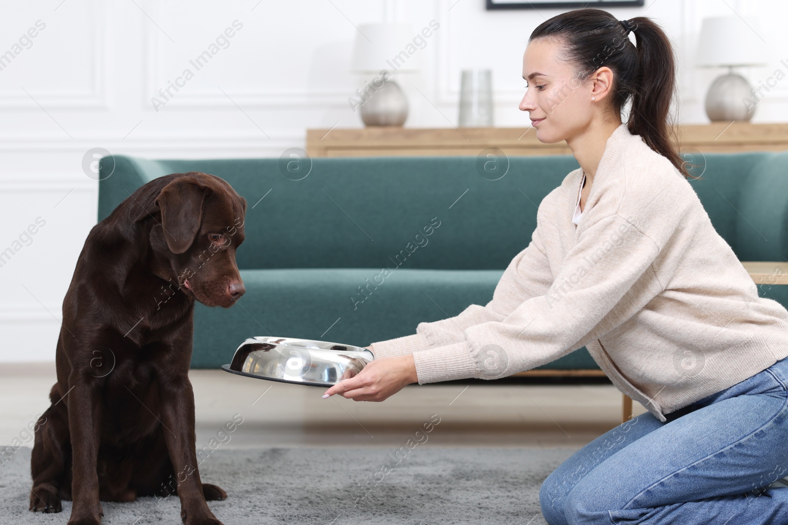 Photo of Woman giving bowl with dry pet food to her dog indoors