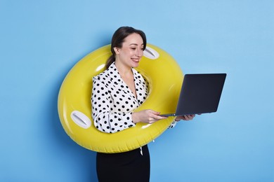 Photo of Businesswoman with inflatable ring and laptop on light blue background