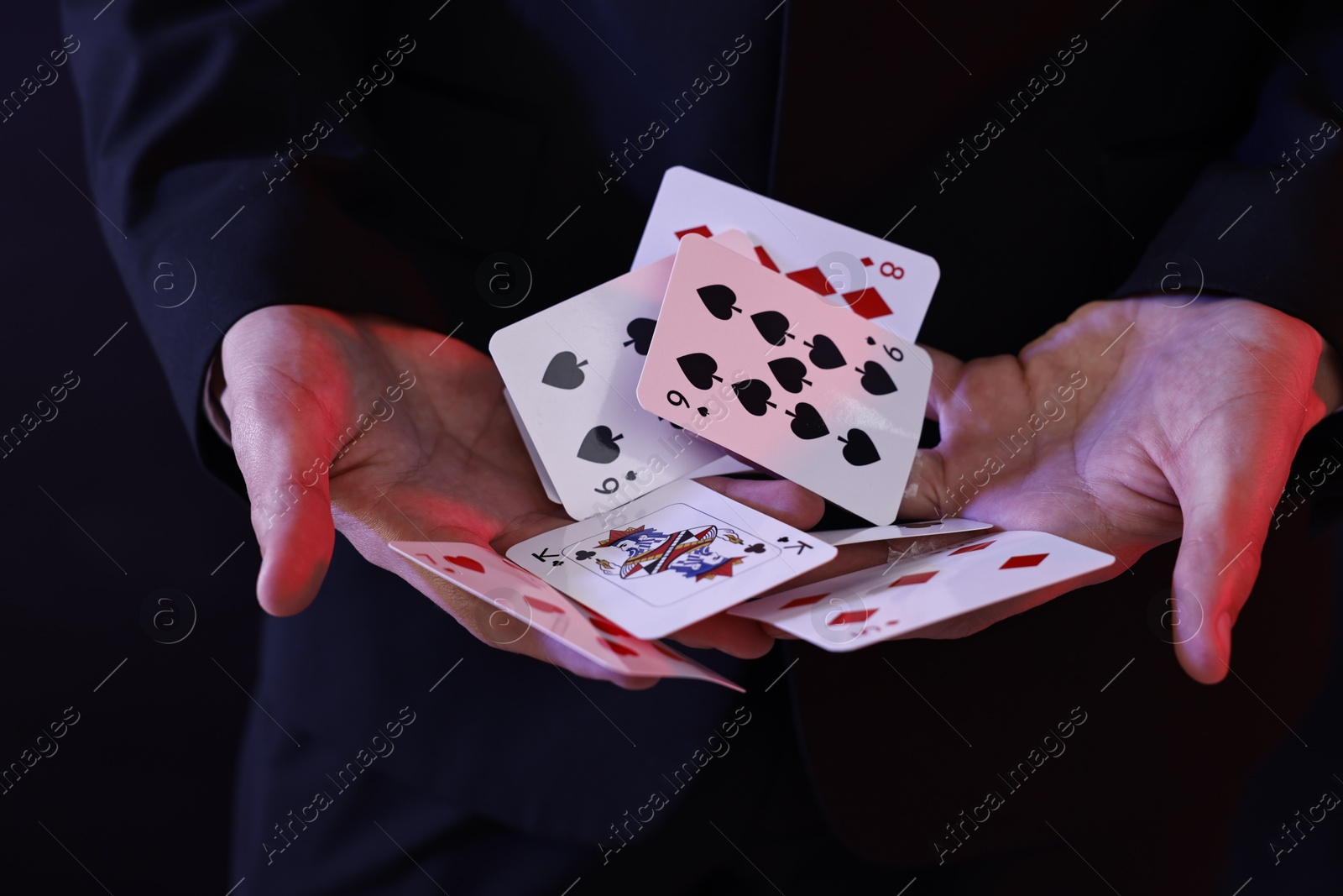 Photo of Illusionist showing trick with playing cards on dark background, closeup