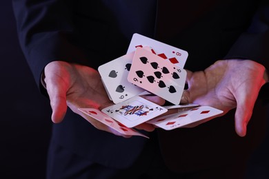 Photo of Illusionist showing trick with playing cards on dark background, closeup