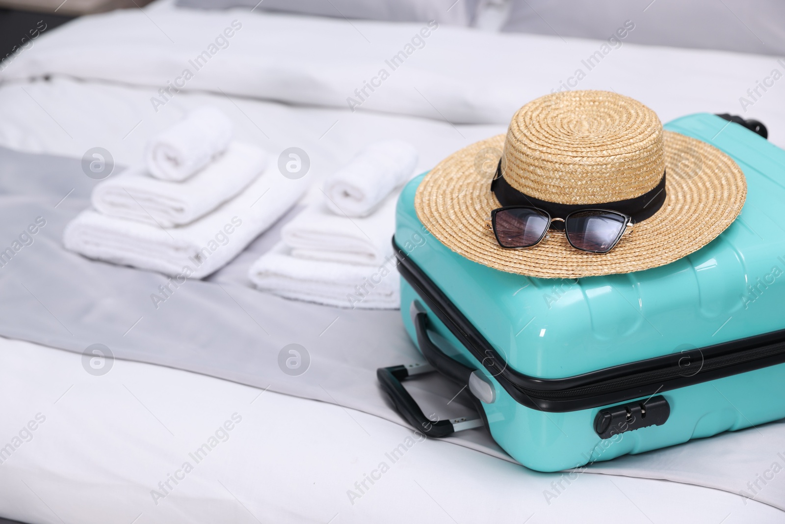 Photo of Suitcase with hat and sunglasses on bed in hotel room, closeup