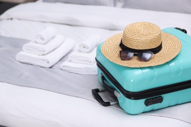 Photo of Suitcase with hat and sunglasses on bed in hotel room, closeup