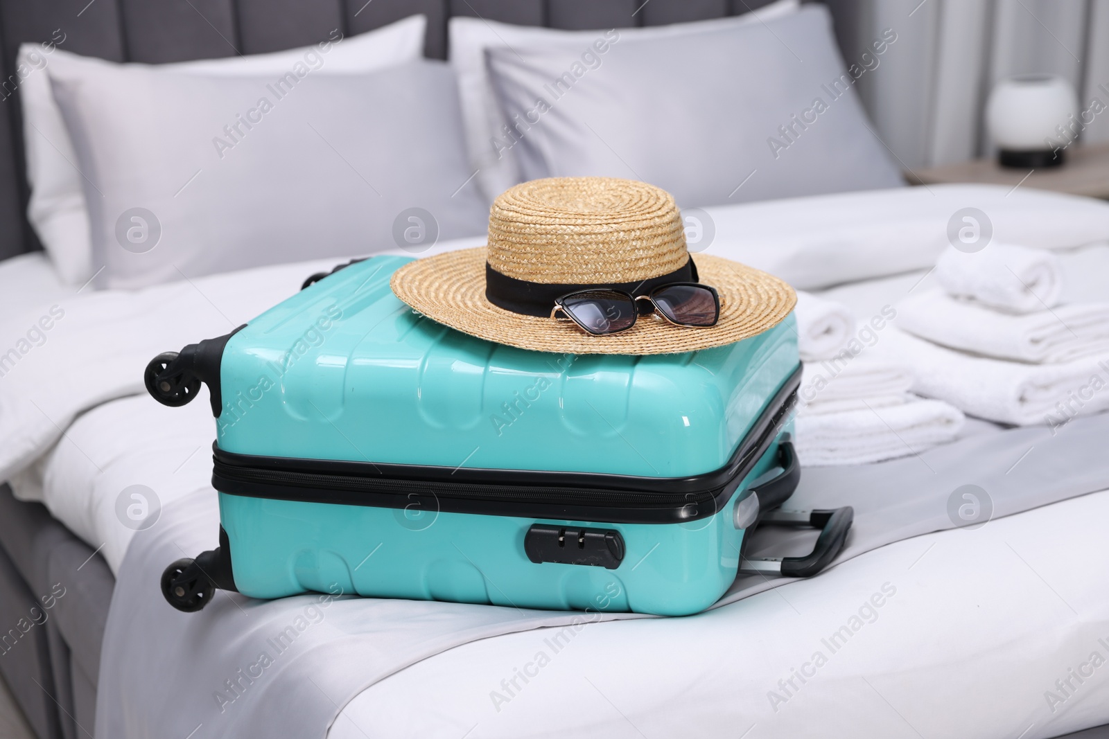 Photo of Suitcase with hat and sunglasses on bed in hotel room, closeup