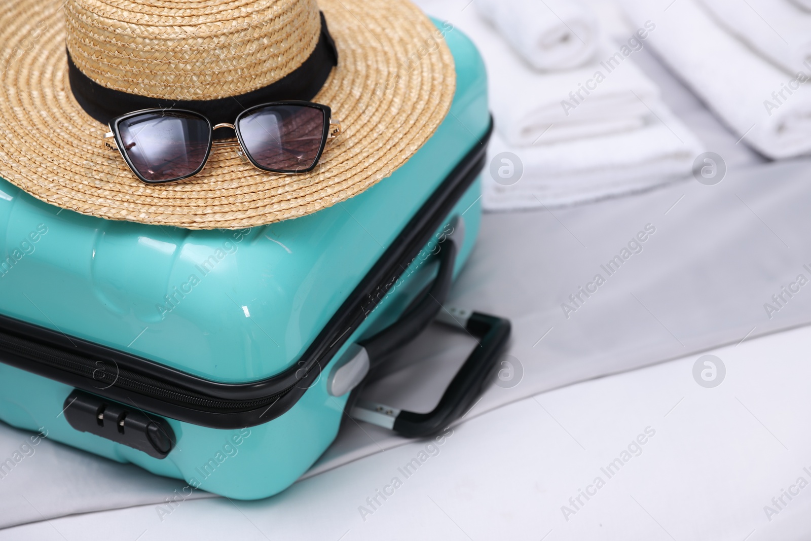 Photo of Suitcase with hat and sunglasses on bed in hotel room, closeup