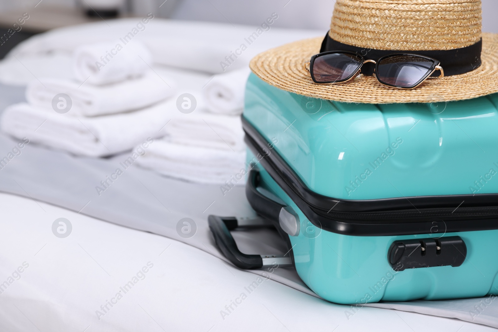 Photo of Suitcase with hat and sunglasses on bed in hotel room, closeup