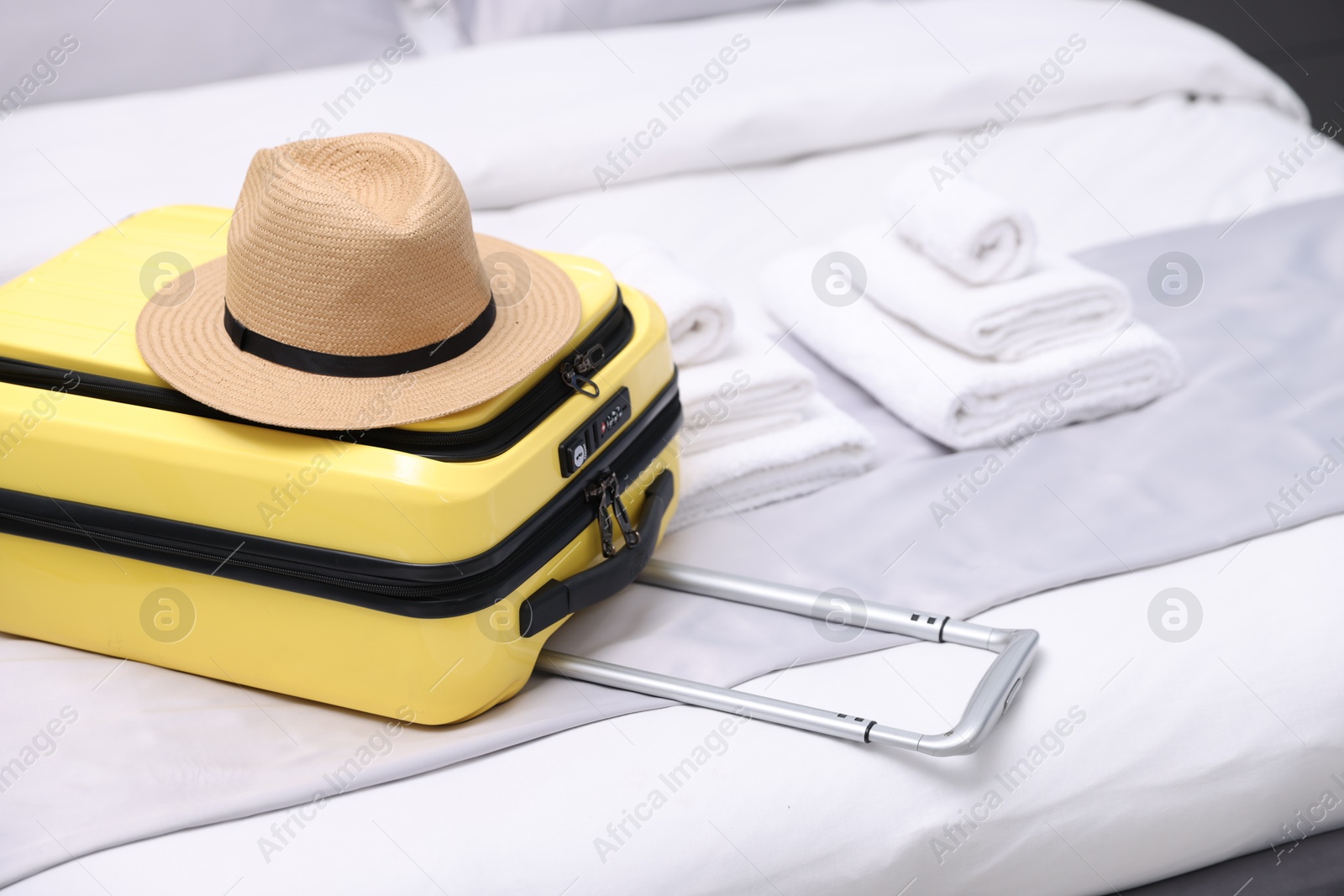 Photo of Suitcase with hat on bed in hotel room, closeup